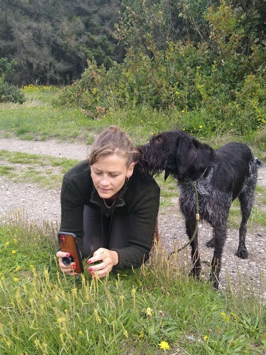 Gunhild beim Pflanzenfotografieren in der Wiese mit Braja daneben