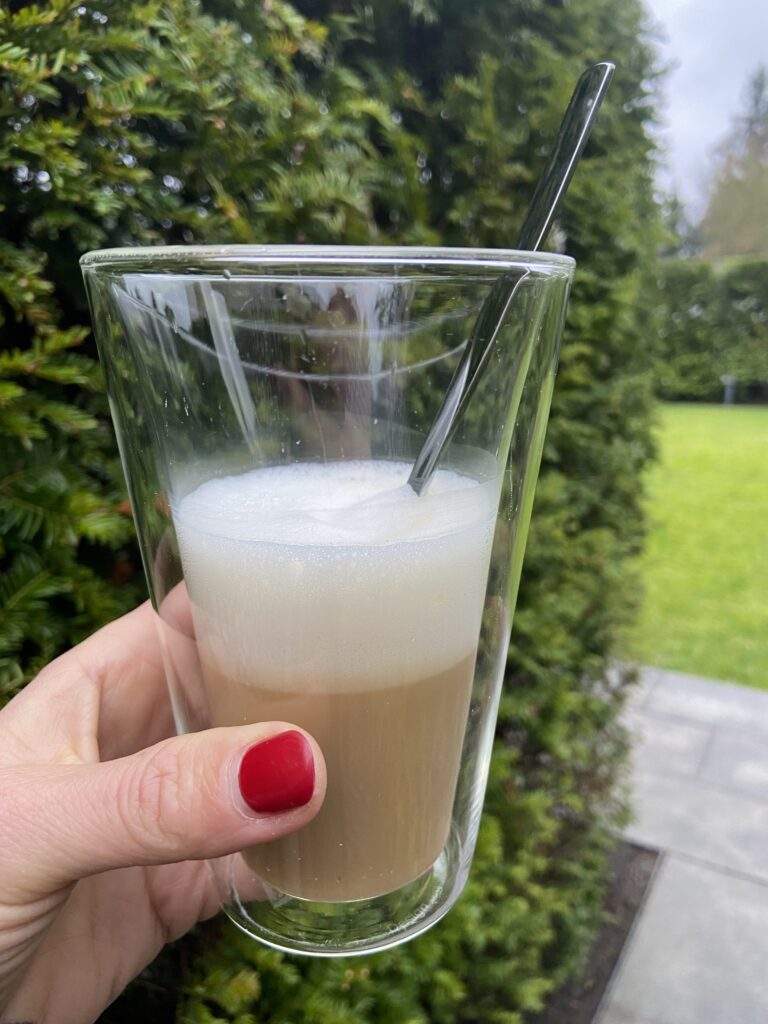 Latte macciato im Isolierglas vor immergrüner Hecke