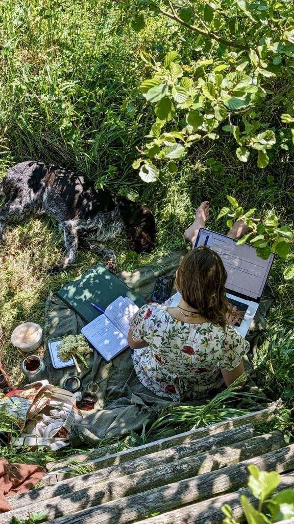 Gunhild Rudolph sitzt am Fuße einer Kanzel in der Natur auf einer Decke und arbeitet.