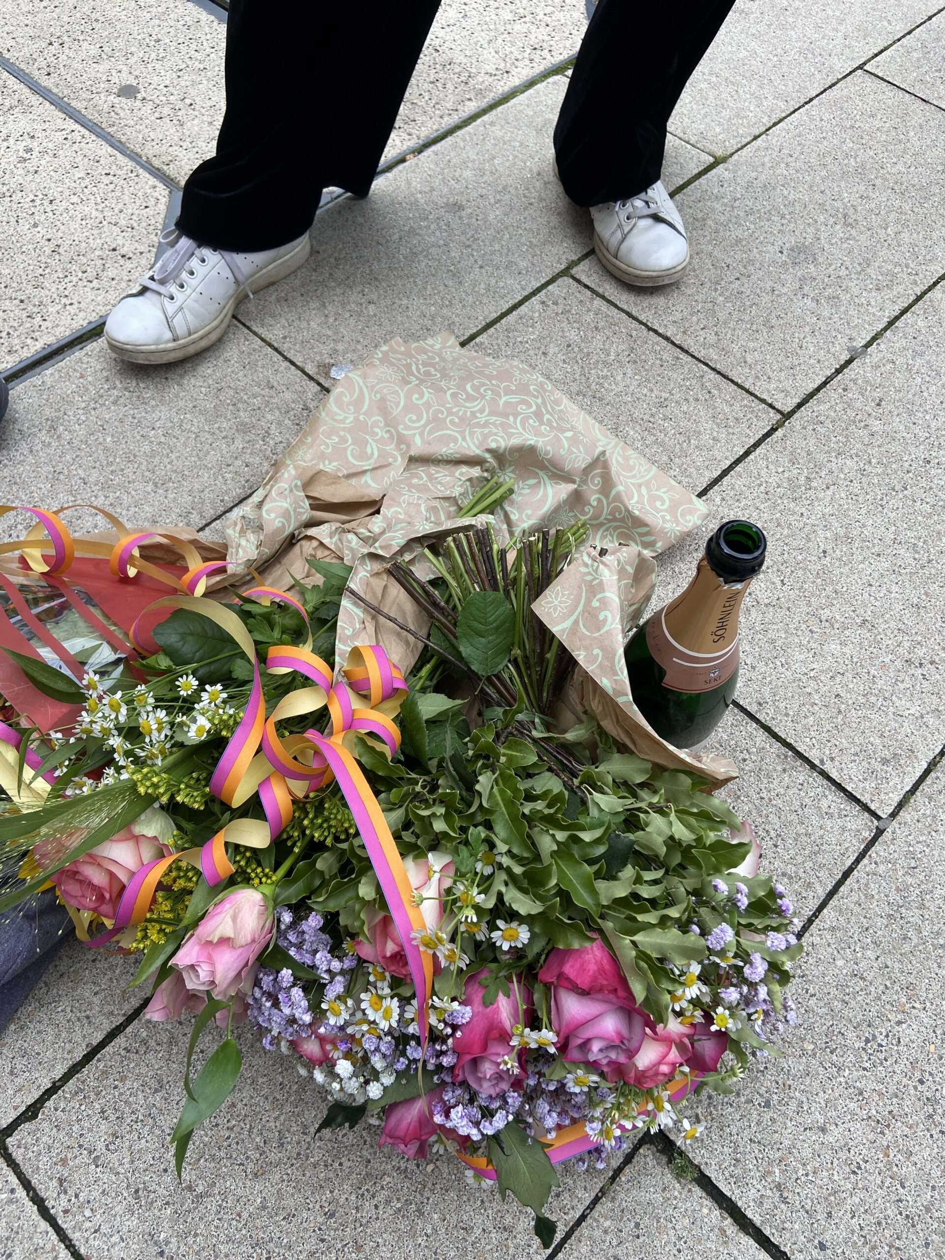 Blumenstrauß und Sekt auf dem Bürgersteig