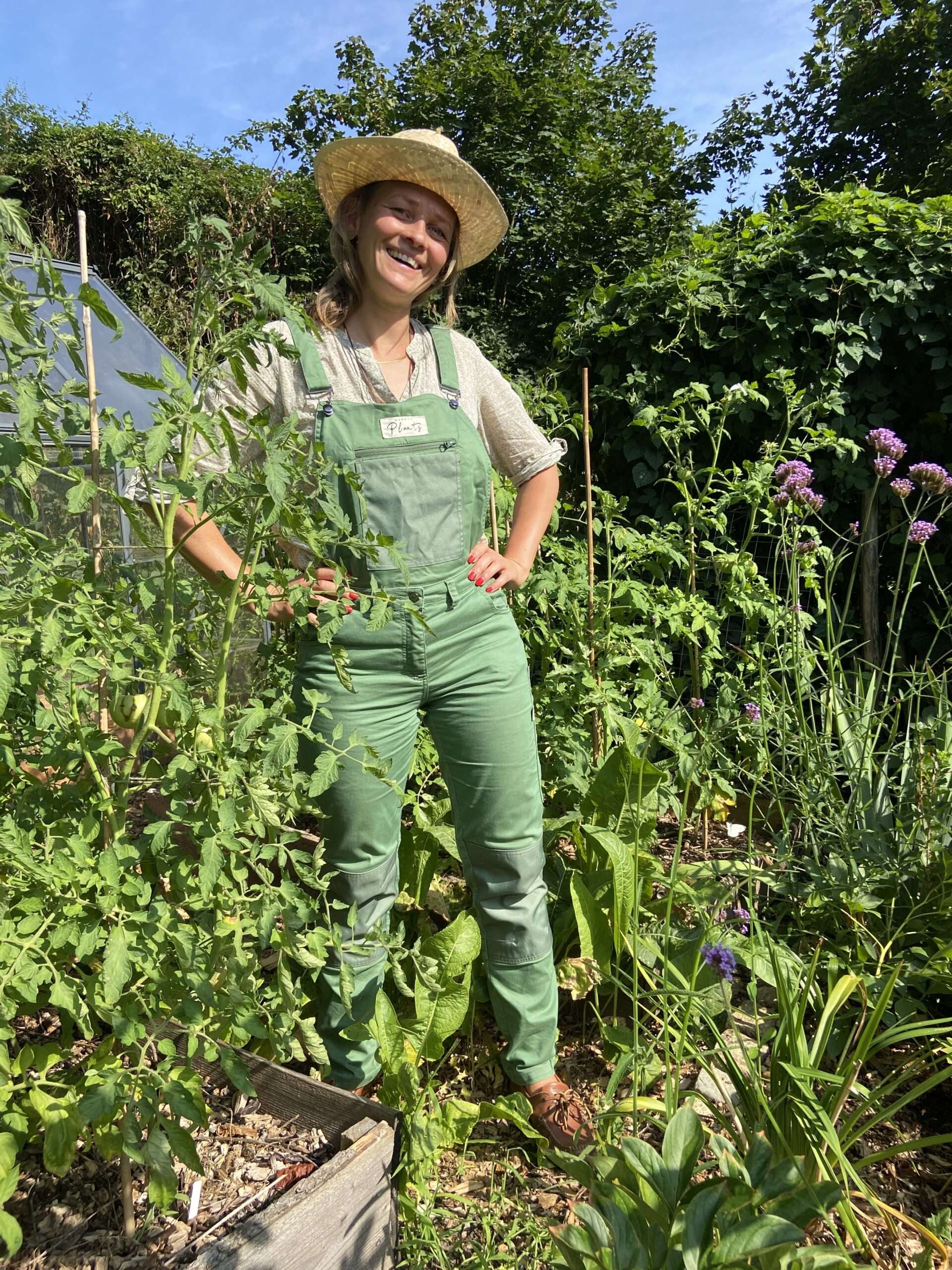 selbstbewusste, lachende Gunhild im Garten mit Händen an der Hüfte.