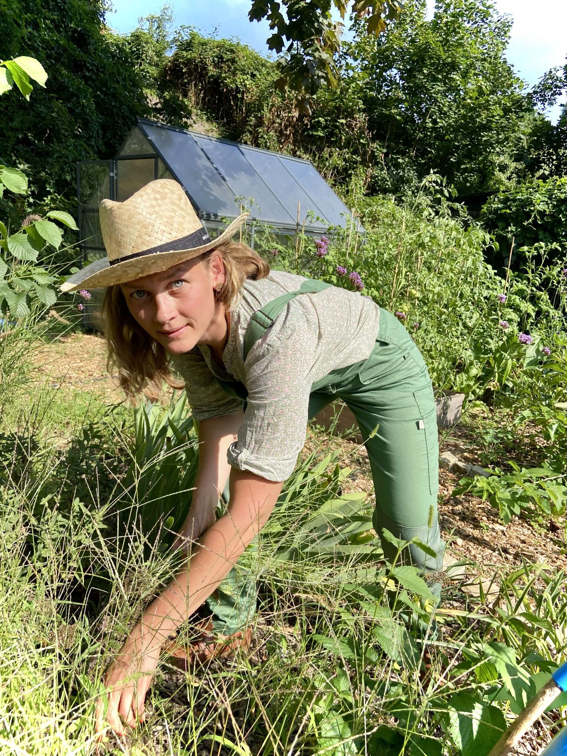 Gunhild Rudolph mit Gartenhose und Strohhut über ein Beet gebeugt