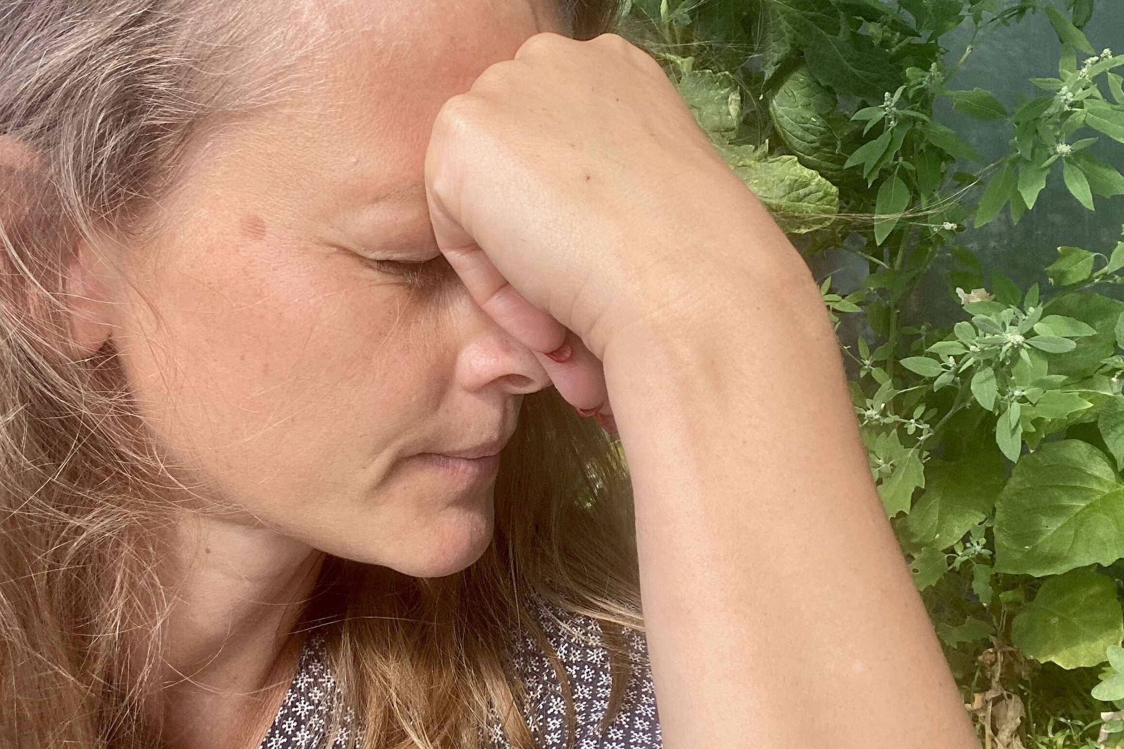Gunhild stützt im Garten den Kopf in die Hand.
