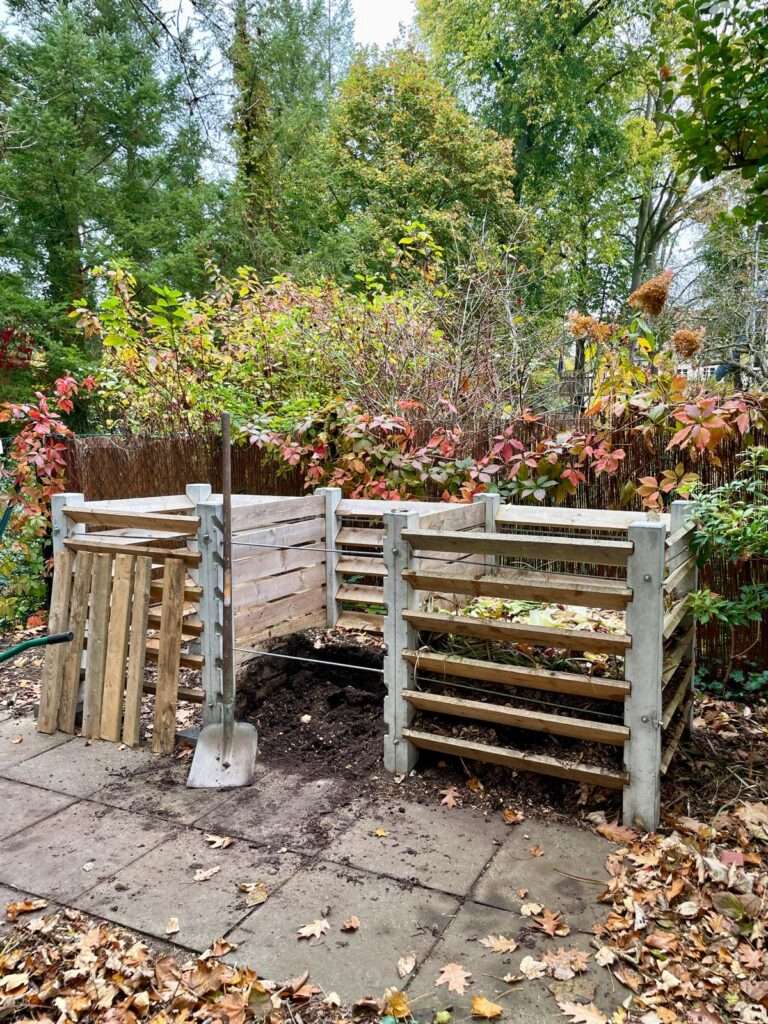 Ein hölzerner Komposter in einem herbstlichen Garten.
