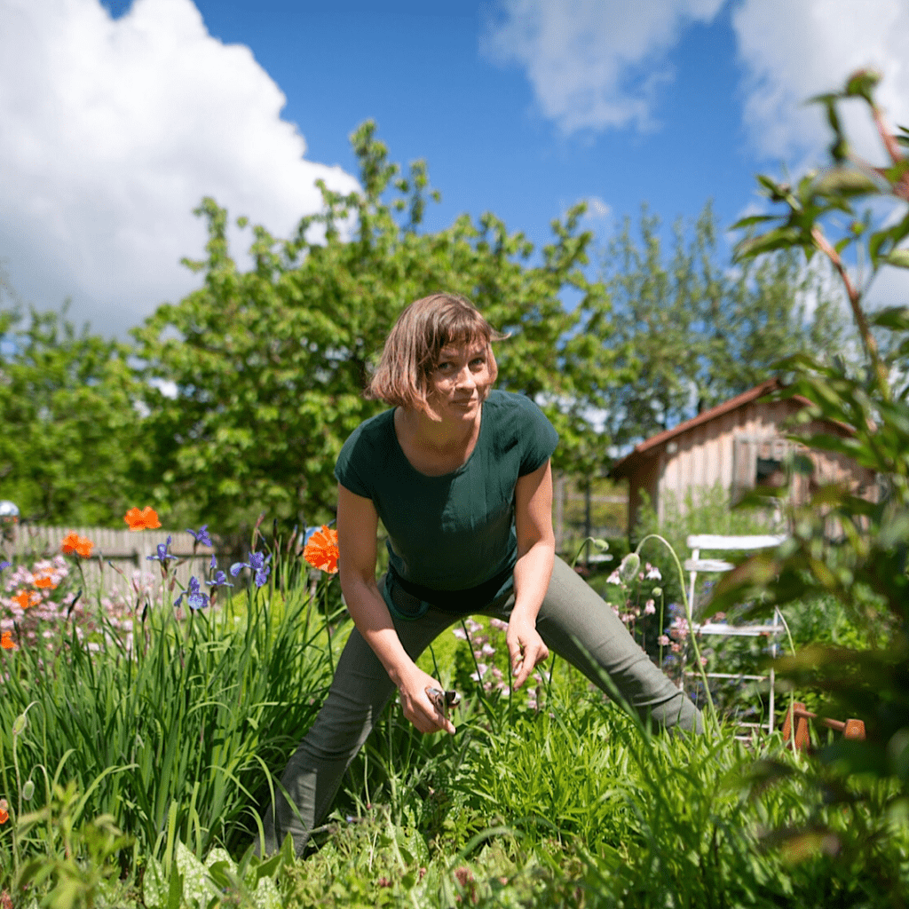 Gunhild Rudolph im grünen Oberteil arbeitet in einem blühenden Garten.