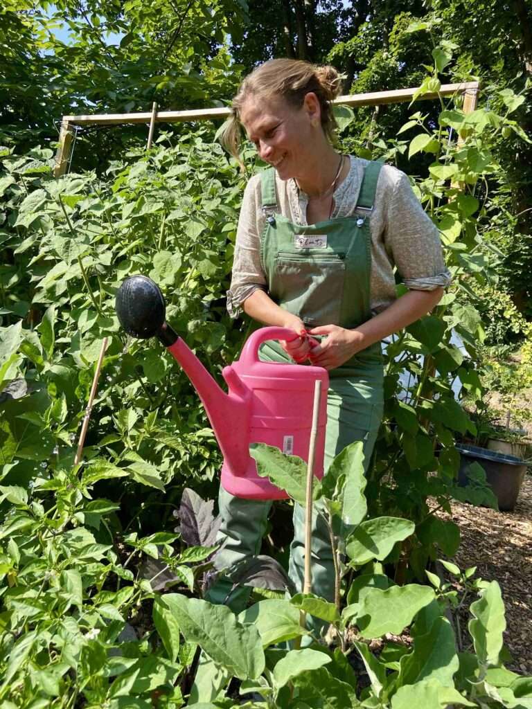 Gunhild Rudolph gießt mit einer pinken Gießkanne die Pflanzen im Garten.